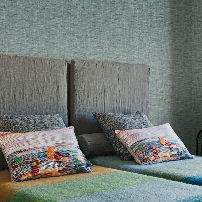 Sfeervolle slaapkamer met Missoni behang uit de Tweed-collectie en kleurrijke sierkussens op een bed met grijze hoofdborden.