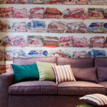 Paarse bank met gekleurde kussens voor Pierre Frey behang FP319001 met een motief van opgevouwen dekens.