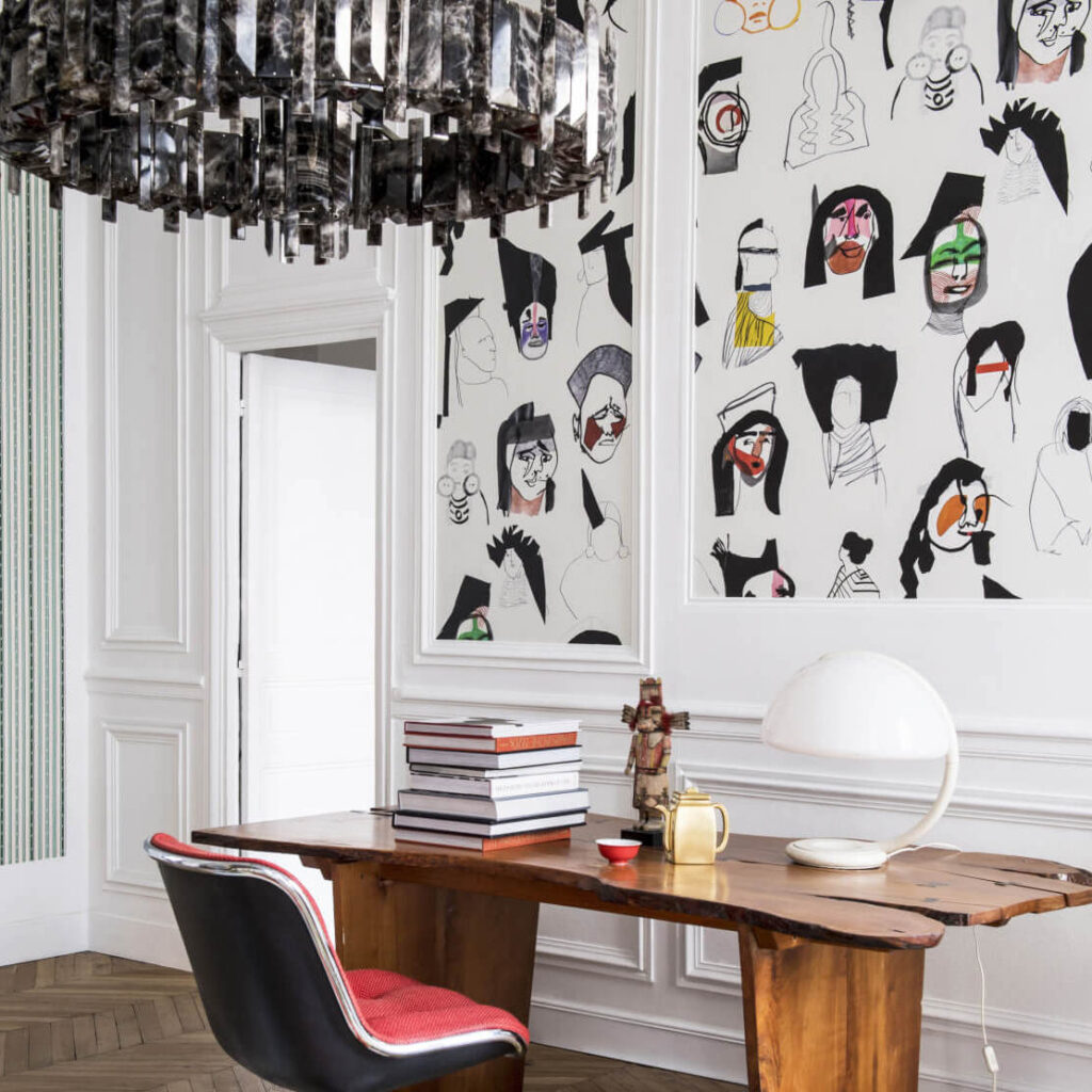 Hedendaags interieur met Pierre Frey behang ‘Shaman’ vol abstracte gezichten achter een houten bureau.