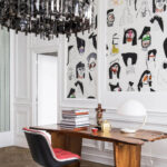 Hedendaags interieur met Pierre Frey behang ‘Shaman’ vol abstracte gezichten achter een houten bureau.