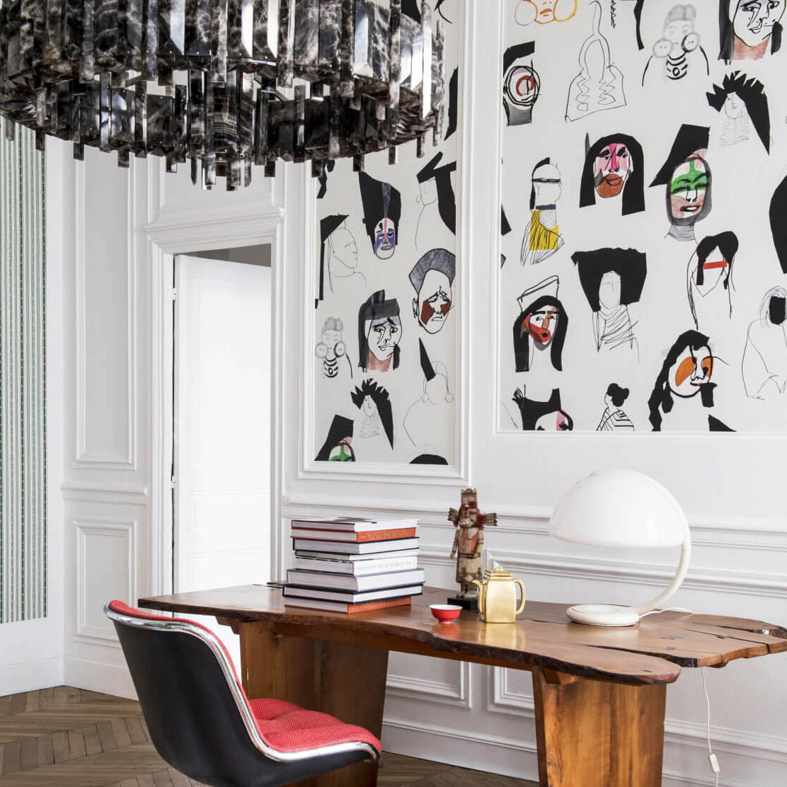 Hedendaags interieur met Pierre Frey behang ‘Shaman’ vol abstracte gezichten achter een houten bureau.