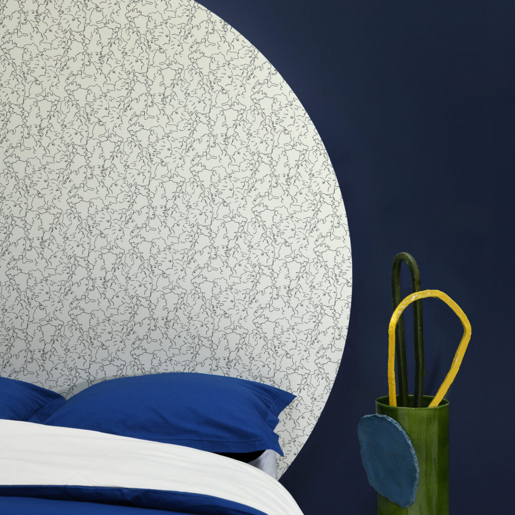 Slaapkamer met opvallend RESSEMBLANCE-behang in een grote cirkelvorm op een donkerblauwe muur, gecombineerd met blauw beddengoed en een groene vaas met decoratieve objecten.