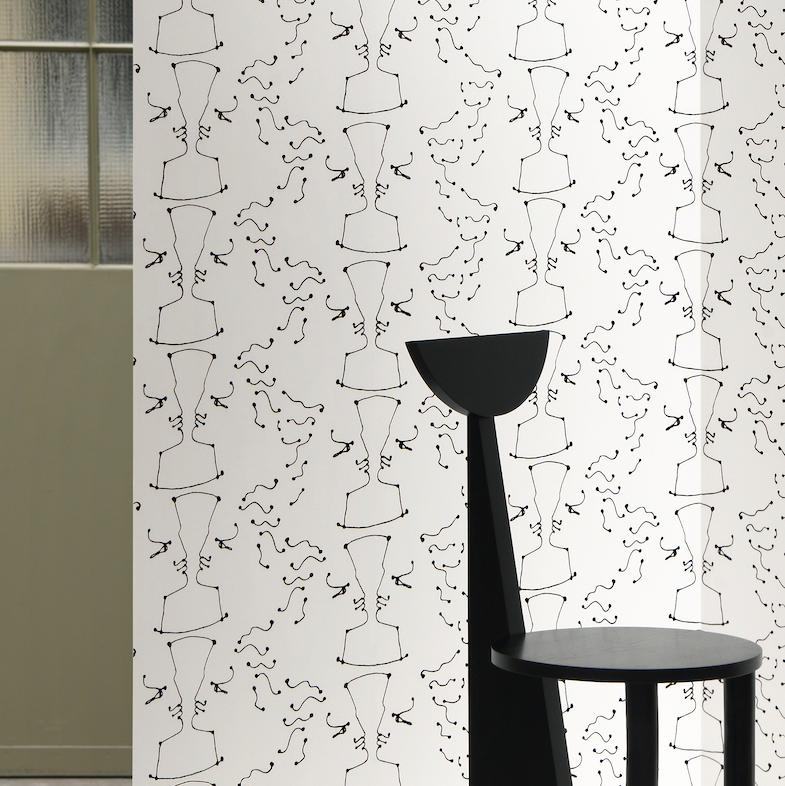 Wit behang met een herhalend abstract lijnpatroon van tegenovergestelde gezichten, genaamd TÊTE À TÊTE, met een zwarte designstoel op de voorgrond.