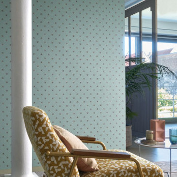 Stijlvol interieur met CASAMANCE Apis-behang in lichtblauw met subtiel patroon, naast een retro fauteuil en grote ramen.