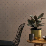 Modern interieur met CASAMANCE Apis 2-behang met bijenmotief, een plant in een gouden pot en een zwarte designstoel.