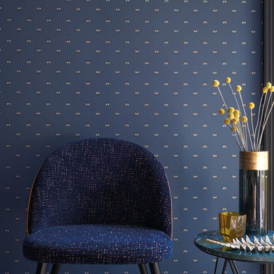 Donkerblauwe wand met CASAMANCE Apis-behang met een bijenpatroon, gecombineerd met een blauwe stoel en decoratief bijzettafeltje.