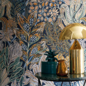 Behang met kleurrijk botanisch patroon uit de CASAMANCE BORROMÉE collectie, gecombineerd met een gouden tafellamp en glazen accessoires op een marmeren tafel.