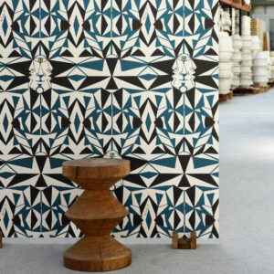 Geometrisch behang met abstracte gezichten en blauw-zwarte patronen in een industriële ruimte, met een houten kruk ervoor.