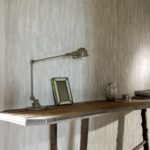 Houten tafel met industriële lamp, fotolijst en accessoires tegen een muur bekleed met Belitung-VP-723-01 behang.