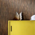 Geel kastje met decoraties tegen een donkerbruine Belitung-VP-723-07 houtstructuurbehangmuur.