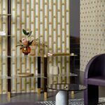 Modern interieur met Biseau Arte behang in goud en wit geometrisch patroon, gecombineerd met glazen meubels en paarse accenten.