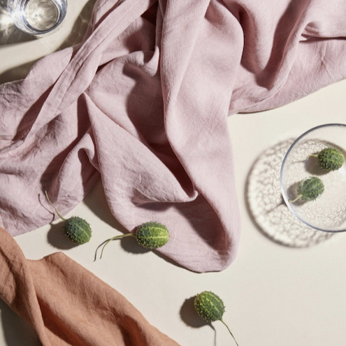 Roze linnen Gracie-tafelkleed van Broste Copenhagen in een sfeervolle setting met decoratieve groene vruchten en glazen.