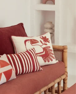 Decoratieve kussens met rode vogel- en streepprints op een rotan bank met rood zitkussen.