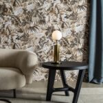 Modern interieur met Buningh Arte Antigua Tropicali behang, een ronde beige fauteuil, zwarte bijzettafel en een lamp met ronde witte kap.