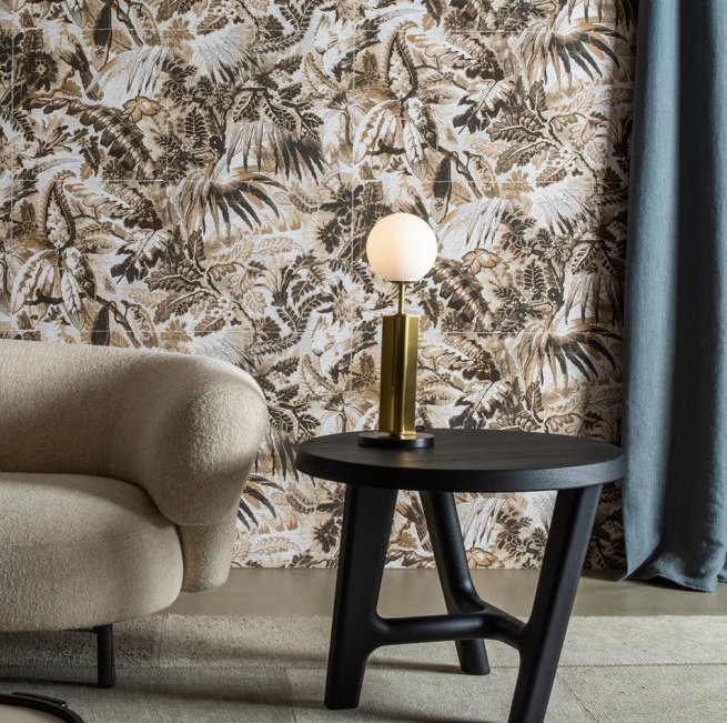 Modern interieur met Buningh Arte Antigua Tropicali behang, een ronde beige fauteuil, zwarte bijzettafel en een lamp met ronde witte kap.