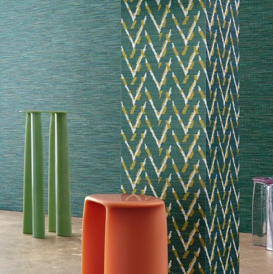 Interieur met Buningh Arte Chasu behang in groen- en blauwtinten, met een oranje kruk en groene bijzettafel.
