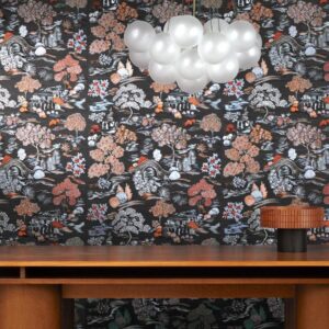Behang met een kleurrijk Japans tuindessin uit de Arte "Gardens of Okayama"-collectie achter een houten tafel en moderne hanglamp.