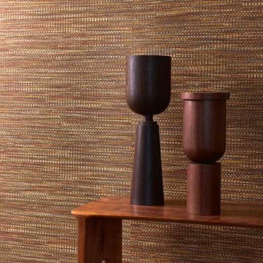 Twee houten decoratieve objecten op een houten tafel voor Buningh Arte Geloma behang met een warm, geweven structuurpatroon.