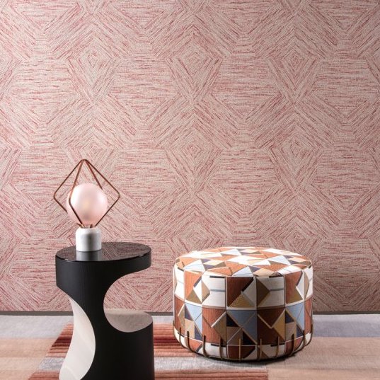 Moderne interieursetting met Buningh Arte Pentagono 33046 behang uit de Antigua collectie, een decoratieve poef met geometrisch patroon en een design bijzettafel met lamp.