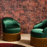 Twee donkergroene fluwelen fauteuils met goudkleurige franjes staan voor een rijkbloemig Buningh-Arte-Stagionato-33011 behang uit de Antigua-collectie.