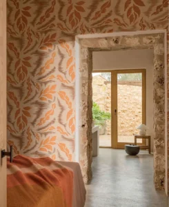 Interieur met Buningh-behang met een natuurprint in aardetinten, een stenen deuropening en zicht op een zonnige patio.