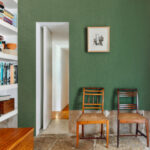 Interieur met groene Buningh Elitis Lin VP 953 31 wandbekleding, twee houten stoelen, een boekenplank en een kunstwerk aan de muur.