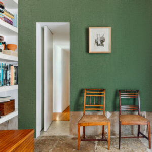 Interieur met groene Buningh Elitis Lin VP 953 31 wandbekleding, twee houten stoelen, een boekenplank en een kunstwerk aan de muur.