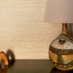 Decoratieve lamp en houten object voor een wand met Buningh Elitis Ortigia Travertin crème behang.