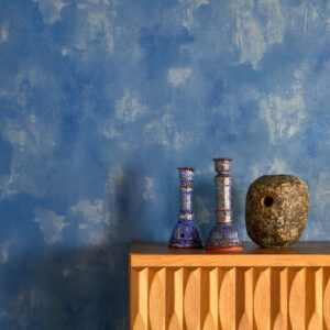 Houten kast met decoratieve objecten tegen een blauw gemarmerd Buningh-Elitis Ortigia Agrigente behang.