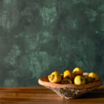 Houten schaal met gele appels op een houten tafel, voor groen Buningh Elitis Ortigia Agrigente behang.