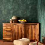 Houten dressoir tegen een donkergroene Ortigia Agrigente-behangmuur met decoratieve vazen en een schaal met fruit.