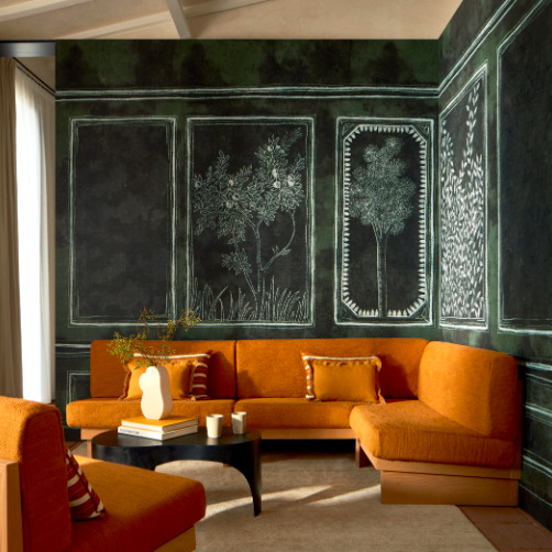 Woonkamer met oranje hoekbank en Buningh Elitis Ortigia panorama behang met getekende bomen op een donkere achtergrond.
