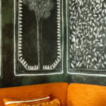 Detail van de Buningh Elitis Ortigia Disegno VP 961 01 wandbekleding met witte botanische tekeningen op een donkere achtergrond, boven een oranje bank.