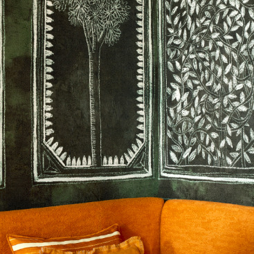 Detail van de Buningh Elitis Ortigia Disegno VP 961 01 wandbekleding met witte botanische tekeningen op een donkere achtergrond, boven een oranje bank.