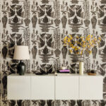 Wand met Buningh-Elitis Paros behang uit de Lin Brodés collectie, met zwart botanisch patroon en een modern wit dressoir met decoratieve accessoires.