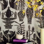 Decoratief Buningh-Elitis Paros behang met zwarte illustraties van vazen, vogels en planten op een lichte achtergrond, gecombineerd met interieuraccessoires en een tak met gele bloemen.
