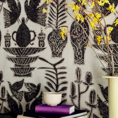 Decoratief Buningh-Elitis Paros behang met zwarte illustraties van vazen, vogels en planten op een lichte achtergrond, gecombineerd met interieuraccessoires en een tak met gele bloemen.