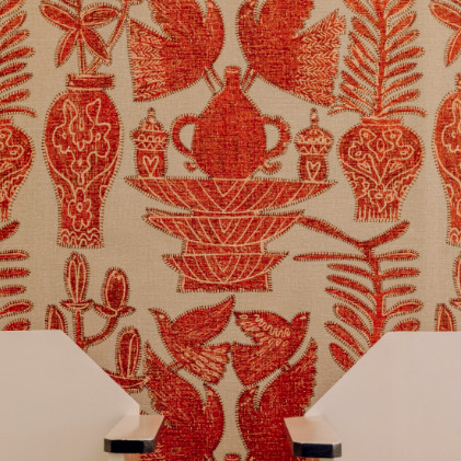 Behang uit de Buningh-Elitis Paros collectie met rood-oranje geborduurde motieven van vogels, vazen en planten op een beige achtergrond.