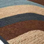 Detail van het Elitis vloerkleed Penny Lane in blauw en aardetinten met golvend patroon.