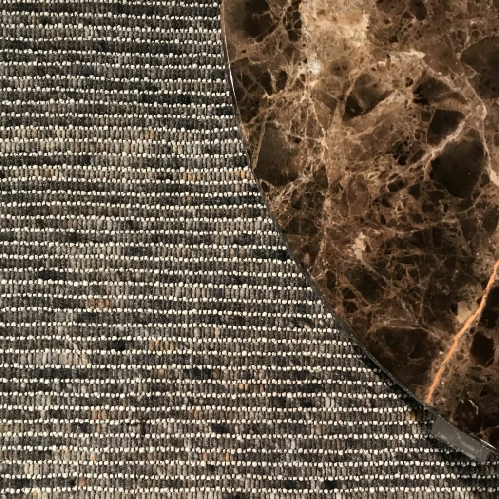 Detail van een Perletta Alp Clay vloerkleed met een rond marmeren tafelblad erop.