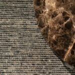 Detail van een Perletta Alp Clay vloerkleed met een rond marmeren tafelblad erop.