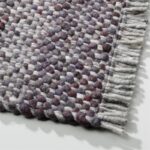 Detail van het Perletta Garno 499-01 vloerkleed met dik geweven structuur in grijs-, paars- en wittinten en franjes aan de rand.