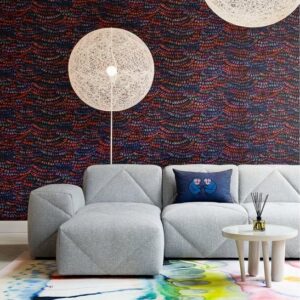 Moderne zithoek met een lichtgrijze designbank, Moooi Dandelion lampen en behang van Arte met een kleurrijk patroon.