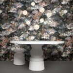 Witte design tafel en kruk voor een donkere, bloemrijke muur met Moooi Memento behang van Arte.