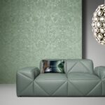 Groen Arte Moooi Mimic Moth behang met bloemenpatroon achter een moderne groene designbank en een decoratieve hanglamp.