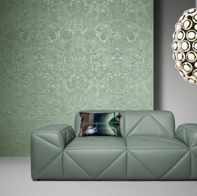 Groen Arte Moooi Mimic Moth behang met bloemenpatroon achter een moderne groene designbank en een decoratieve hanglamp.