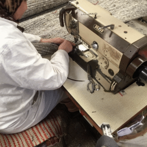 Vakman naait een handgemaakt Perletta vloerkleed met een industriële naaimachine.