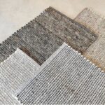 Vier Perletta Alp vloerkleden in neutrale tinten liggen deels overlappend op een lichtgekleurde ondergrond.