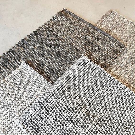 Vier Perletta Alp vloerkleden in neutrale tinten liggen deels overlappend op een lichtgekleurde ondergrond.