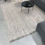 Beige Perletta Doppio vloerkleed in een moderne woonkamer met grijze bank en zwarte salontafel.